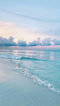 an ocean beach with waves coming in to the shore and clouds over the water at sunset