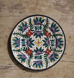 a white plate with colorful designs on it sitting on a wooden table next to a wall