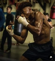 a shirtless man with boxing gloves on his face and hands, standing in a gym