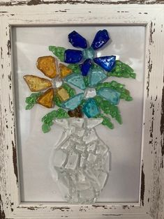 a glass vase filled with lots of different colored flowers inside of a white framed frame