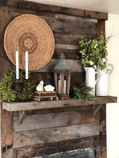 a rustic fireplace mantel decorated with greenery, candles and a wicker basket