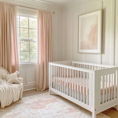 a baby's room with a white crib and pink drapes on the windows