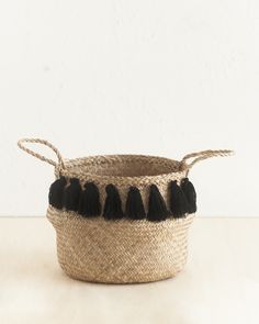 a black and white basket with tassels on the handles sitting on a table