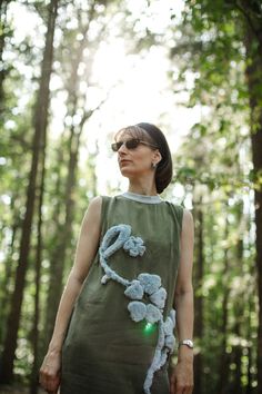 a woman standing in the woods wearing a dress with crocheted flowers on it