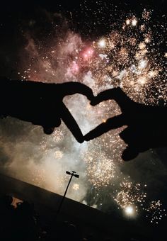 two hands in the shape of a heart with fireworks behind them and a cross at the bottom