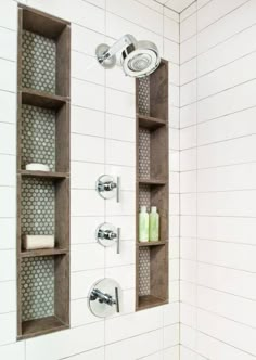 a white tiled shower with shelves above it and soap dispensers on the wall