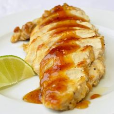 a white plate topped with chicken covered in sauce next to a slice of lime wedge