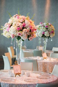 two tall vases filled with pink and white flowers on top of a round table