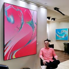 a man sitting on a chair in front of a large art work hanging on the wall