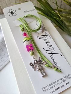 a green bracelet with pink flowers and a cross charm on it, sitting next to a plant