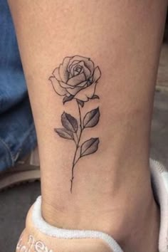 a small rose tattoo on the side of a woman's leg, with leaves