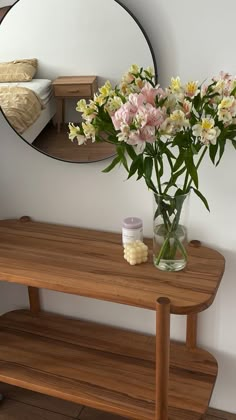 a vase filled with flowers sitting on top of a wooden table next to a mirror