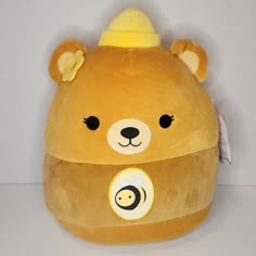 a brown teddy bear with a yellow hat on it's head and eyes, sitting next to a white wall