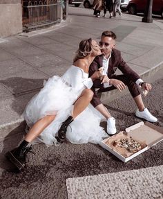 a man and woman dressed in wedding attire sitting on the ground next to an open pizza box