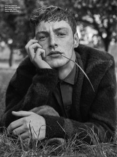 a man sitting in the grass with his hand on his chin and looking at the camera