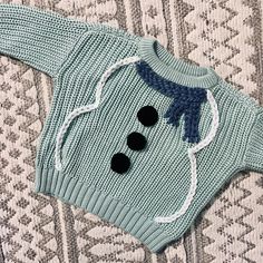 a knitted sweater with buttons on the front and back, sitting on a patterned surface