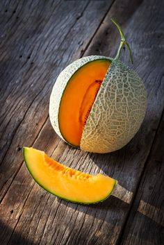 a cantaloupe cut in half sitting on top of a wooden table next to a piece of melon