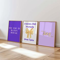 three framed posters on the floor in front of a white wall with purple and yellow lettering