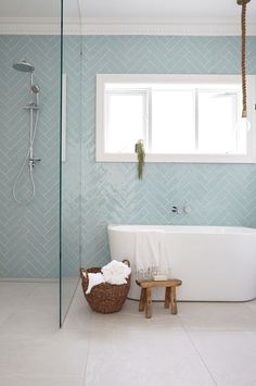 a white bath tub sitting under a window next to a wooden stool in a bathroom