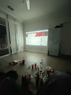 people sitting on the floor in front of a projector screen with drinks scattered around them