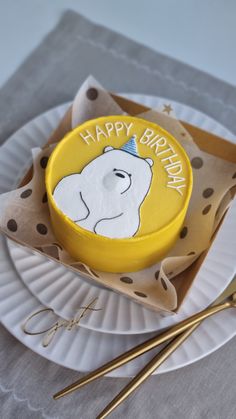 a yellow birthday cake sitting on top of a white plate next to chopsticks