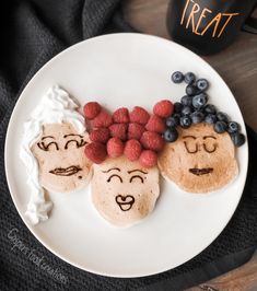 three pancakes with faces drawn on them and berries in the shape of people's heads