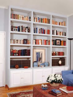 a living room filled with lots of books on top of white bookcases next to a blue couch