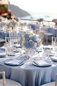 the table is set with blue linens and white flowers in vases on each side