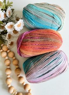 three skeins of yarn next to flowers and beads on a white surface with daisies