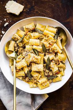 a white bowl filled with pasta and sages on top of a wooden table next to bread