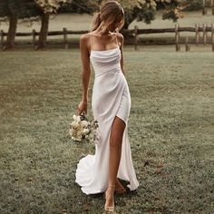 a woman in a white dress holding a bouquet and walking through the grass with her hand on her hip