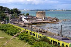 a yellow train traveling down tracks next to the ocean with people standing on top of it