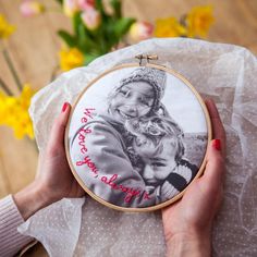 a woman is holding a cross - stitch photo in front of a bouquet of flowers