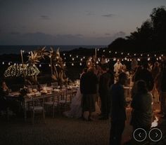 a group of people standing around a table with candles on it at night, surrounded by lights