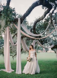 a woman in a wedding dress standing under an arch with draping on it