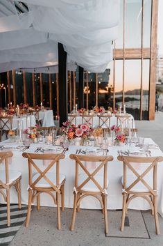 a table set up with white linens and wooden chairs for an outdoor wedding reception