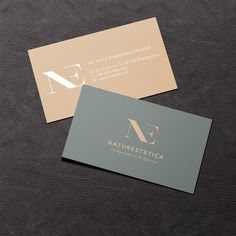 two business cards sitting on top of a black leather surface with gold and silver logos