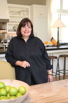 a woman standing in front of a bowl of green apples on a table with chairs