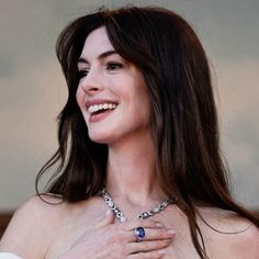 a close up of a person wearing a necklace and smiling at the camera with her hands on her chest