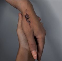 two hands holding each other with a small tattoo on the middle finger and an outline of a rose