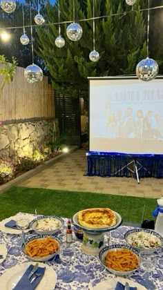 an outdoor movie is set up on the lawn with plates and bowls full of food