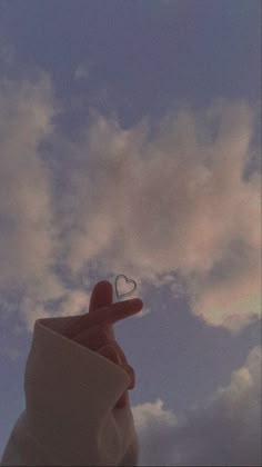 a hand holding a heart shaped object in the sky