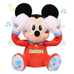 a mickey mouse stuffed animal sitting on top of a white surface with its hands up to his ears