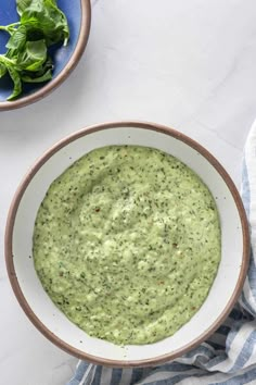 a white bowl filled with green sauce next to a blue and white striped napkin on top of a table