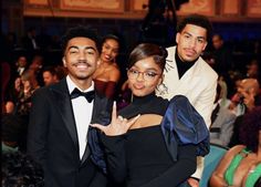 two people standing next to each other in front of a group of people wearing tuxedos