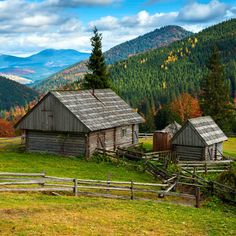 an old barn sits in the middle of a grassy field with mountains in the background