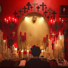 a room with candles and crosses on the wall, in front of a red background