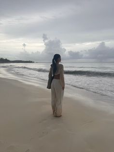 a woman standing on top of a sandy beach next to the ocean under a cloudy sky