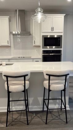 two white stools sit at the center of a kitchen island in front of an oven