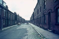 two people walking down an empty street between brick buildings